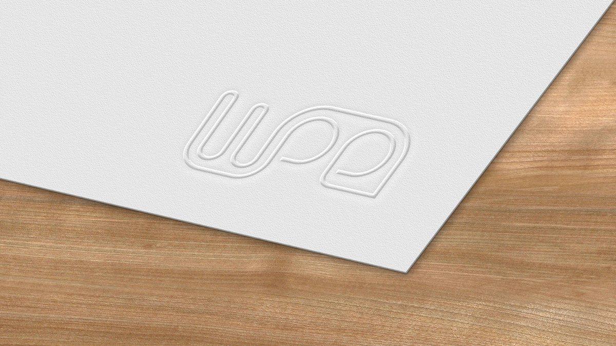 Mock-up of the WPE monogram blind-embossed into a sheet of white paper on a wooden desk